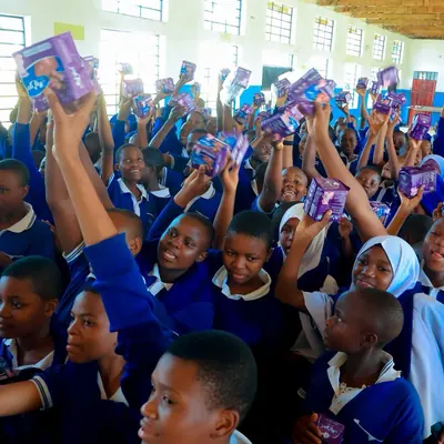 Students at Kafundo Secondary School raising packets of sanitary pads received during a SheRooted distribution