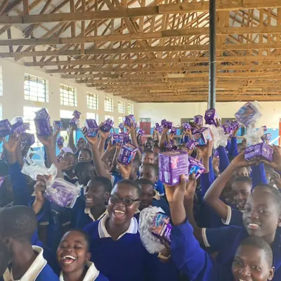 Students holding up sanitary pad packets during a SheRooted distribution in the school hall