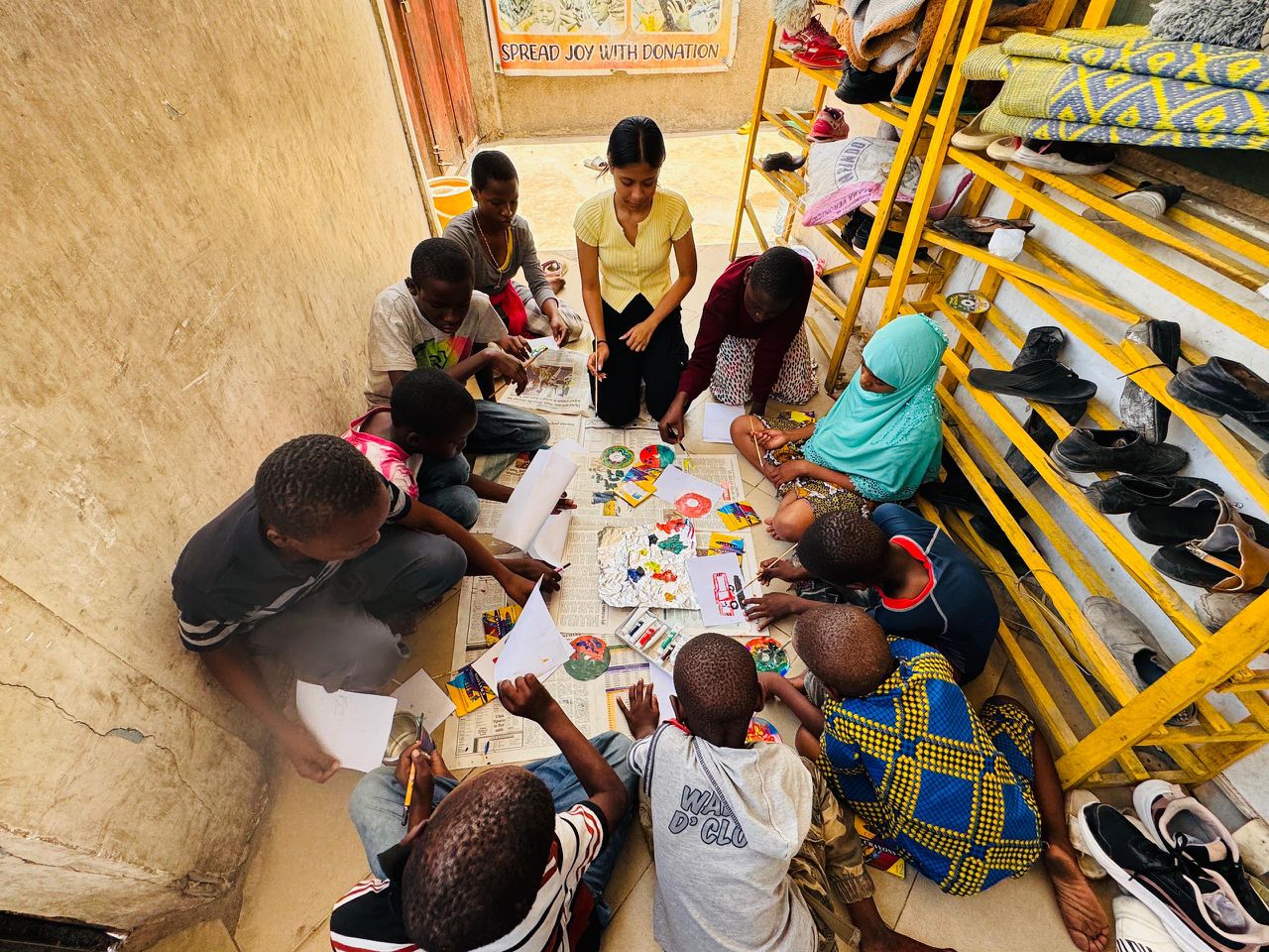 Children sitting on the floor with a volunteer during a colouring activity at Sintanaizer Foundation