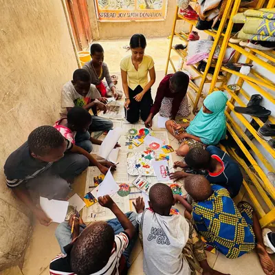 Children sitting on the floor with a volunteer during a colouring activity at Sintanaizer Foundation